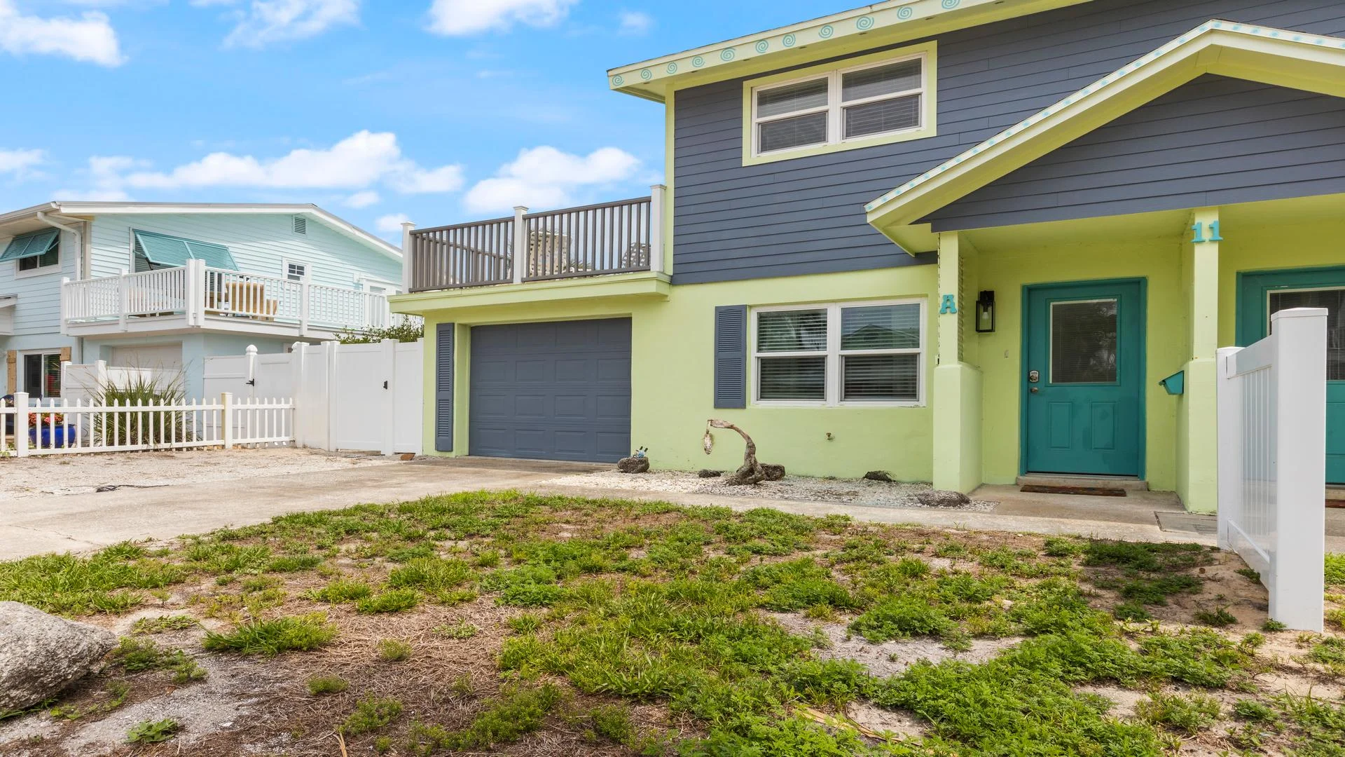 Two-story townhome exterior with blue siding, lime green trim, teal front door, and upper balcony overlooking driveway.