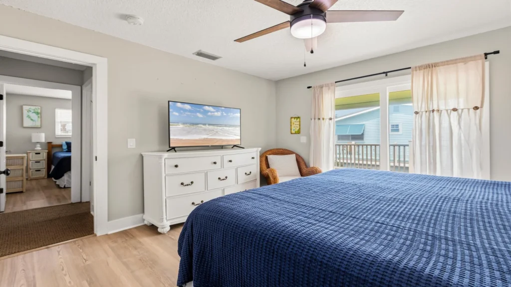 Master bedroom with wood-look flooring, white dresser topped by flat-screen TV, and sliding doors to a balcony.