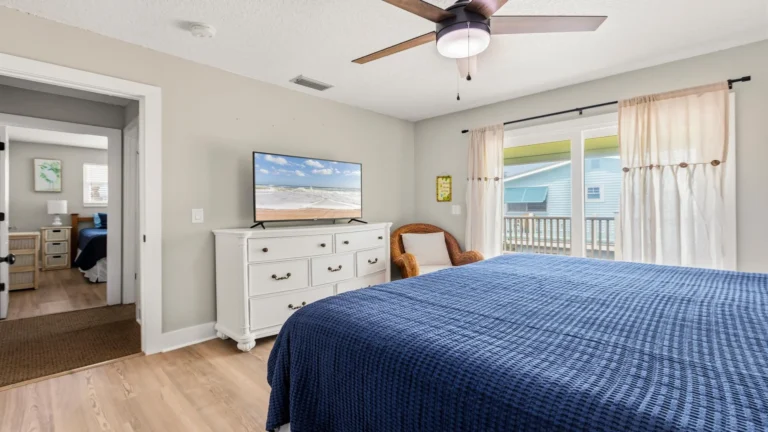 Master bedroom with wood-look flooring, white dresser topped by flat-screen TV, and sliding doors to a balcony.