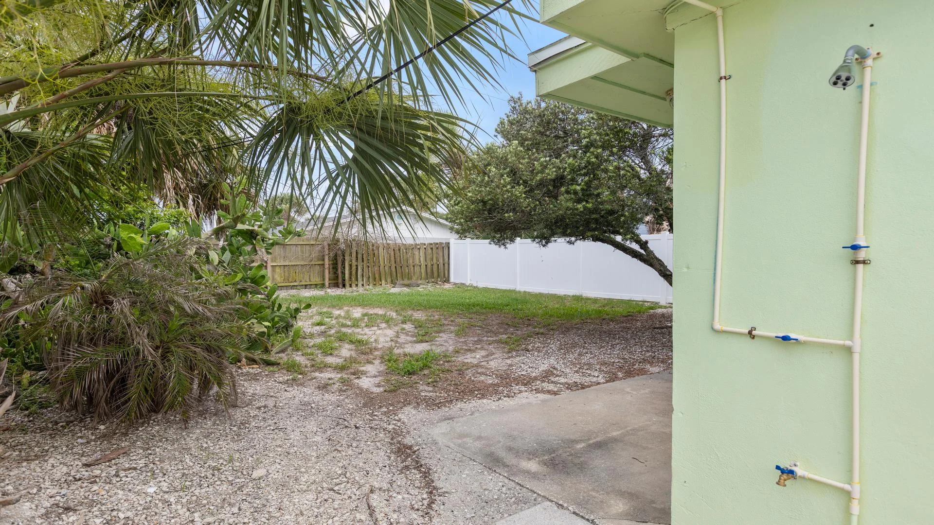 Outdoor shower, gravel path, and fenced backyard with palm trees.