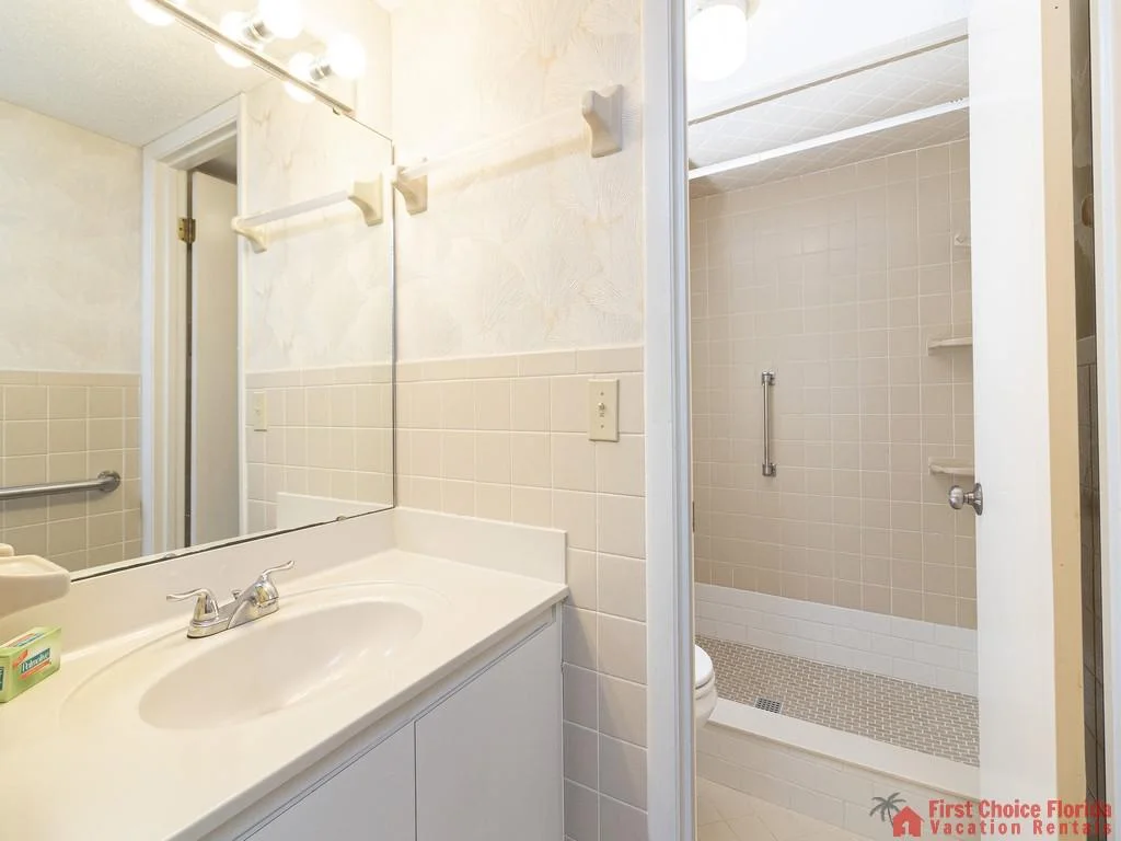 Half bathroom with white vanity, tiled backsplash, and a shower featuring beige square tiles and grab bar.
