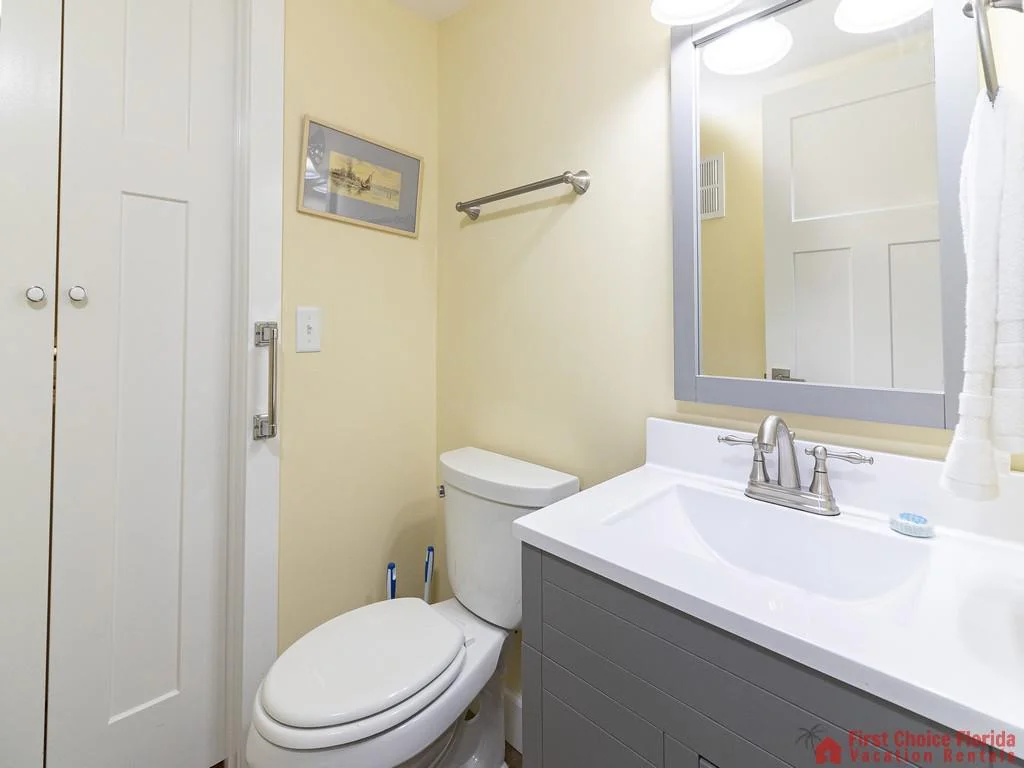 Powder room features a white toilet, gray vanity with quartz countertop, and a framed mirror with overhead lighting.