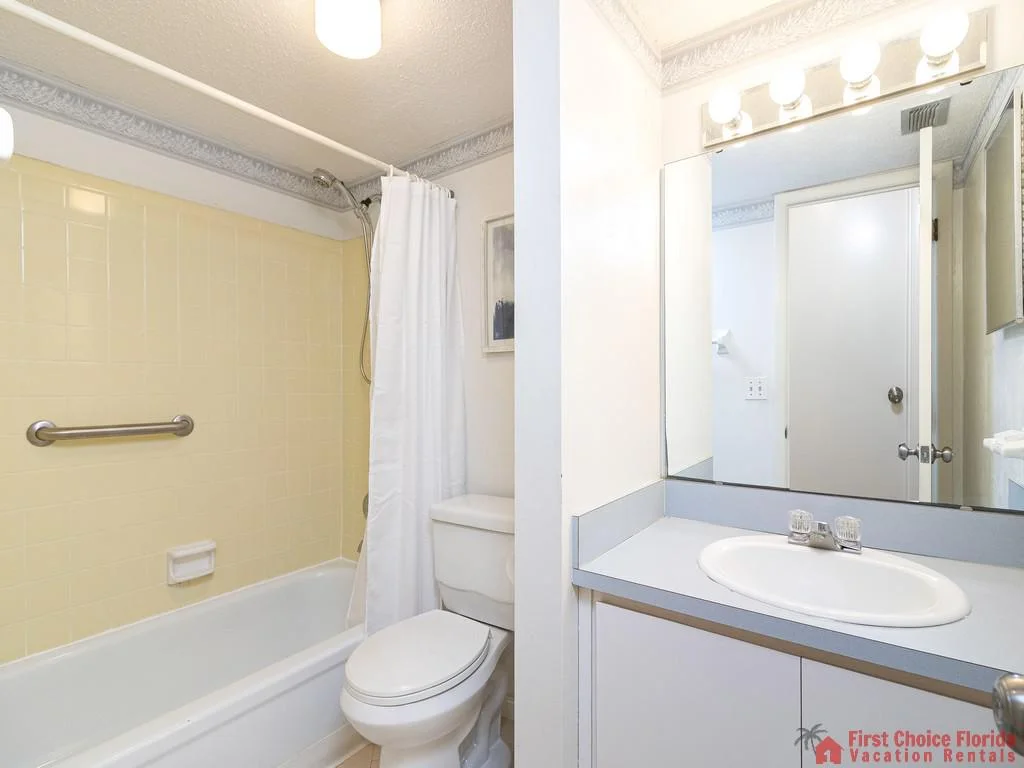 Bathroom with pale yellow tiled tub and shower, white toilet, and a gray countertop with sink beneath a large mirror.