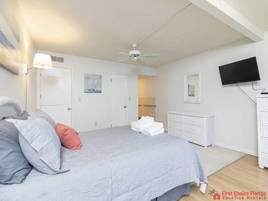 Wall-mounted TV positioned above a white wicker dresser with matching mirror in the queen bedroom.