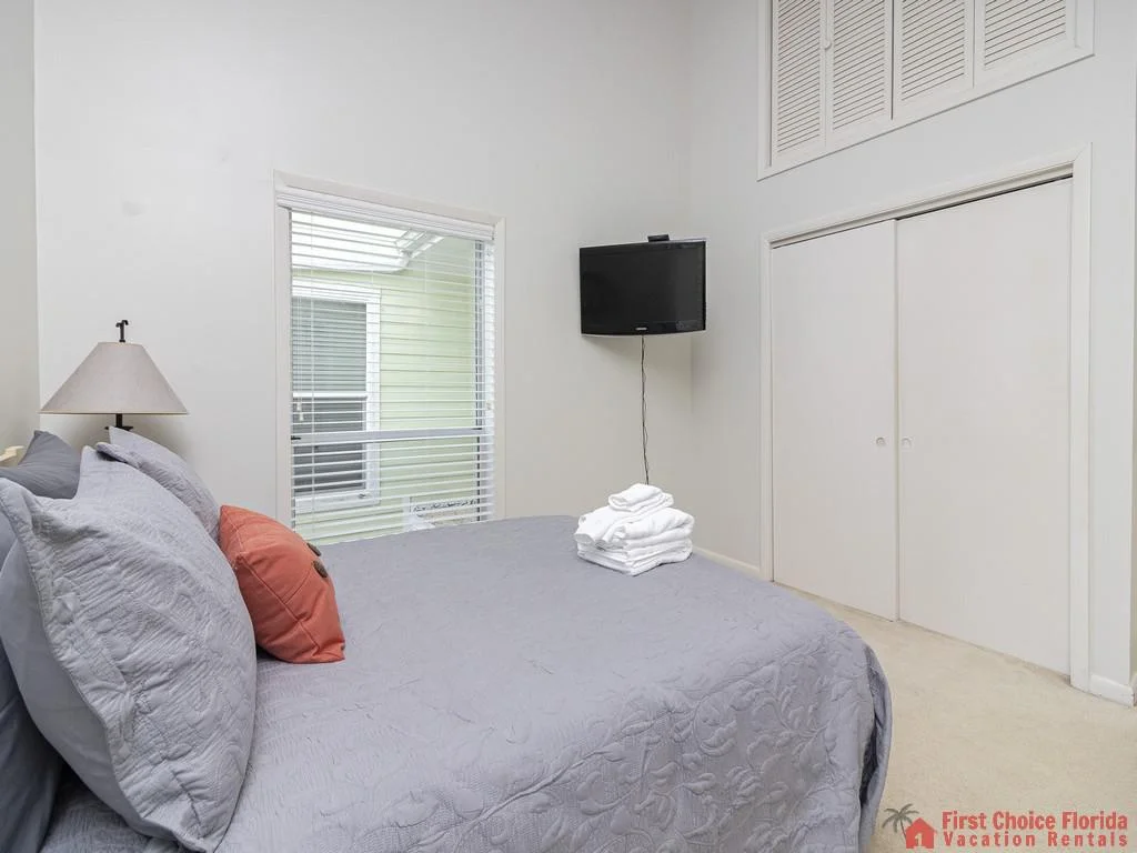 High ceilings and louvered storage doors rise above a queen bed dressed in gray and coral linens.