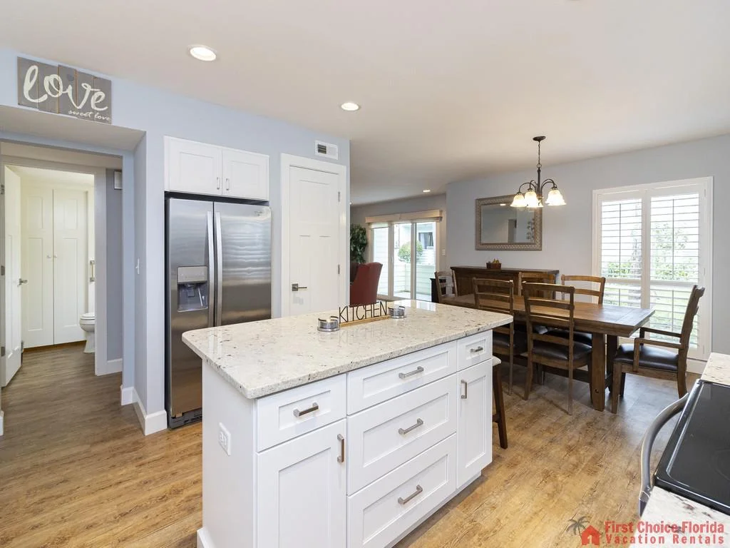 White kitchen island with granite countertop and brushed nickel handles overlooks wooden dining table with eight chairs.
