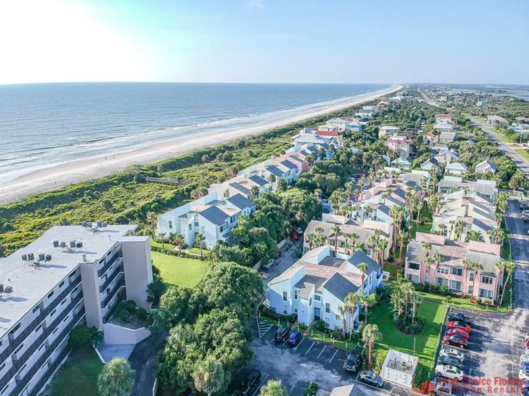Aerial view of coastal townhomes with palm trees lining streets and sandy beach stretching alongside the ocean.