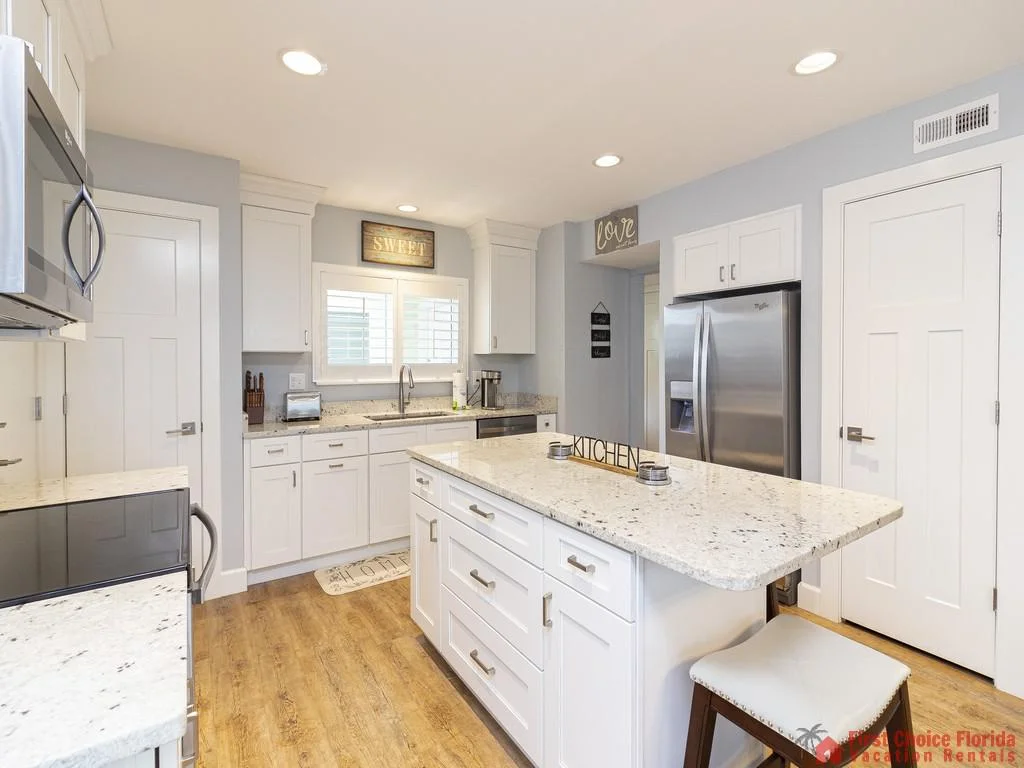 White cabinets and granite counters surround the kitchen island with barstool seating on wood-look flooring.