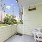 Small tiled patio features white wicker chair and table set beneath a "Pelican Perch" sign.