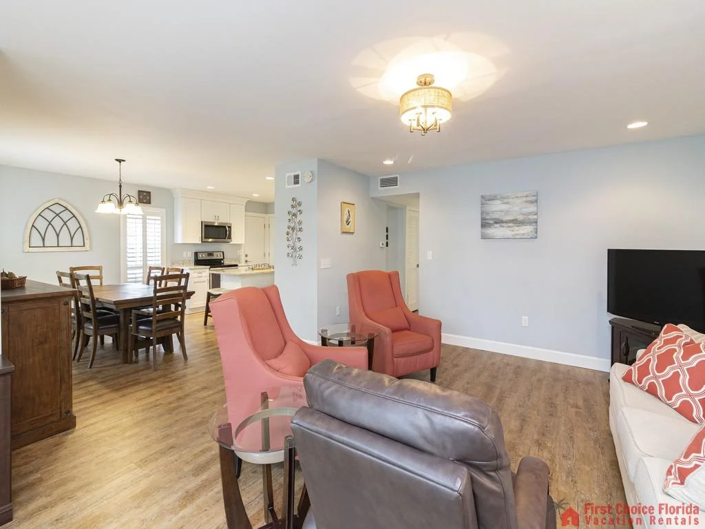 Leather recliner and two coral armchairs face a TV on a dark wood stand in the open living room.