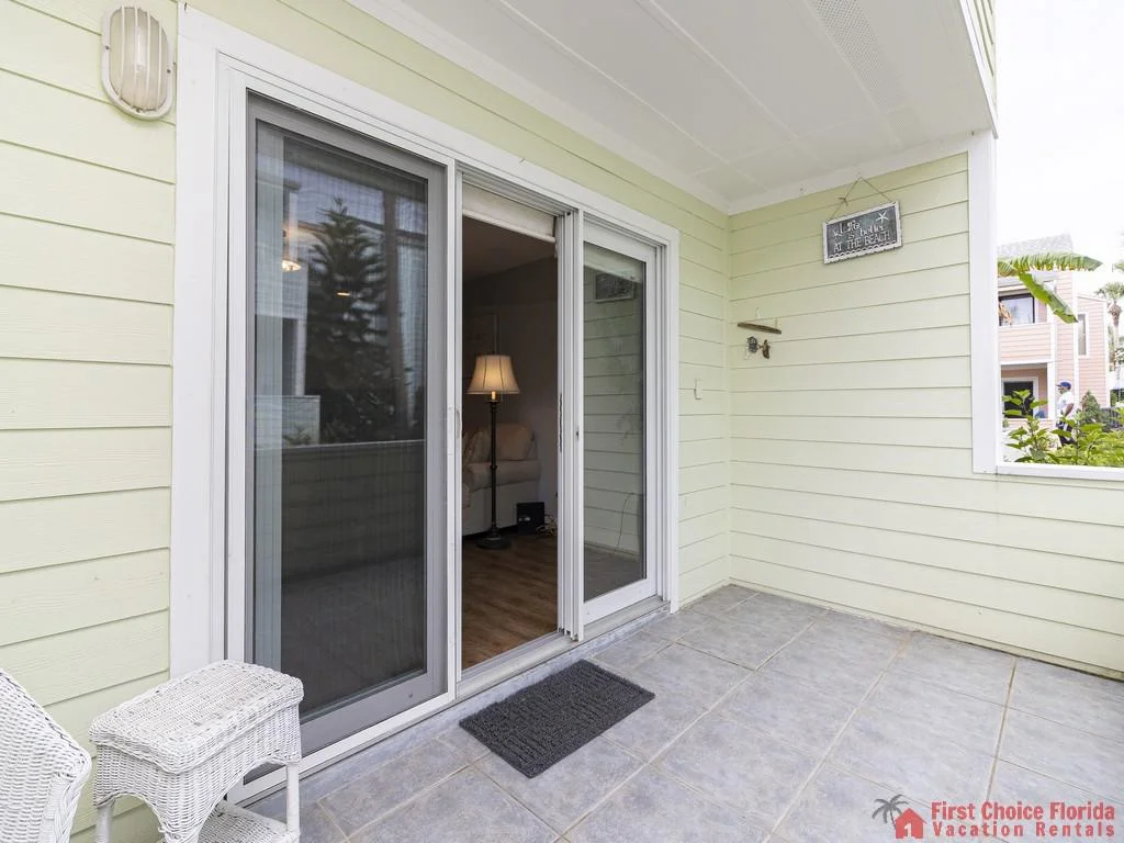 Covered patio with pale yellow siding, gray tiled floor, and sliding glass doors leading indoors.