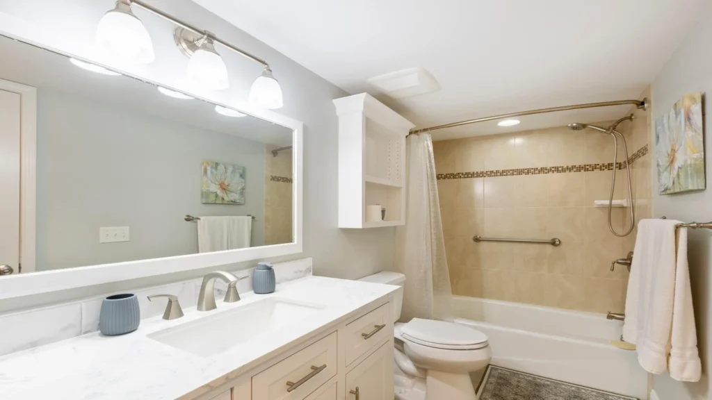Bathroom with marble-look quartz countertop, brushed nickel fixtures, beige tiled tub surround, and white cabinetry.