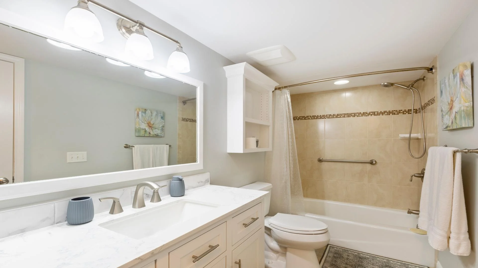 Bathroom with marble-look quartz countertop, brushed nickel fixtures, beige tiled tub surround, and white cabinetry.