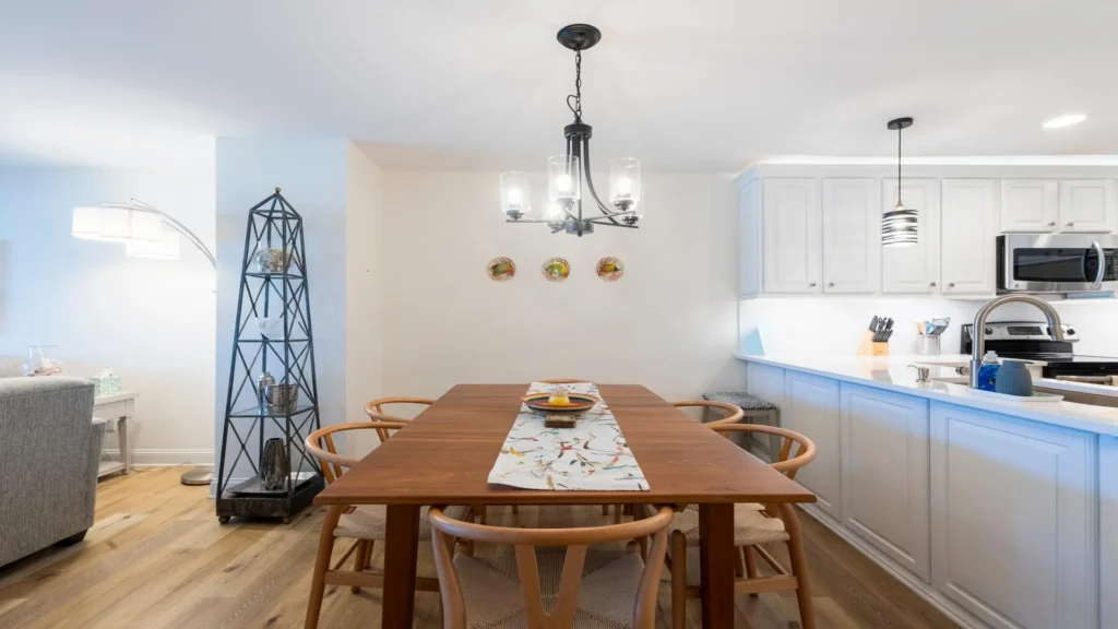 Wood dining table with six woven-seat chairs beneath a black metal chandelier.