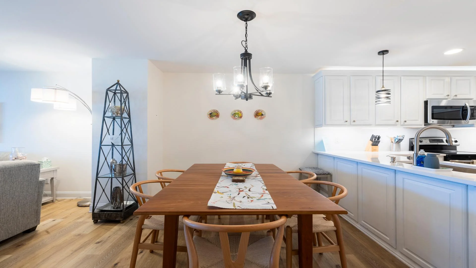 Wood dining table with six woven-seat chairs beneath a black metal chandelier.