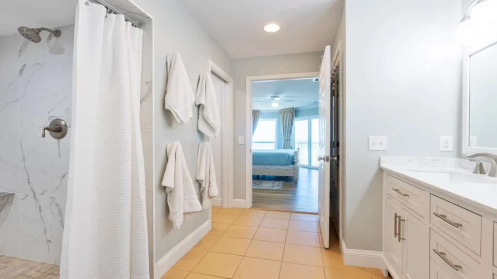 Bathroom with beige tile floor, white cabinetry, marble-look countertop, and a walk-in shower with white curtain.