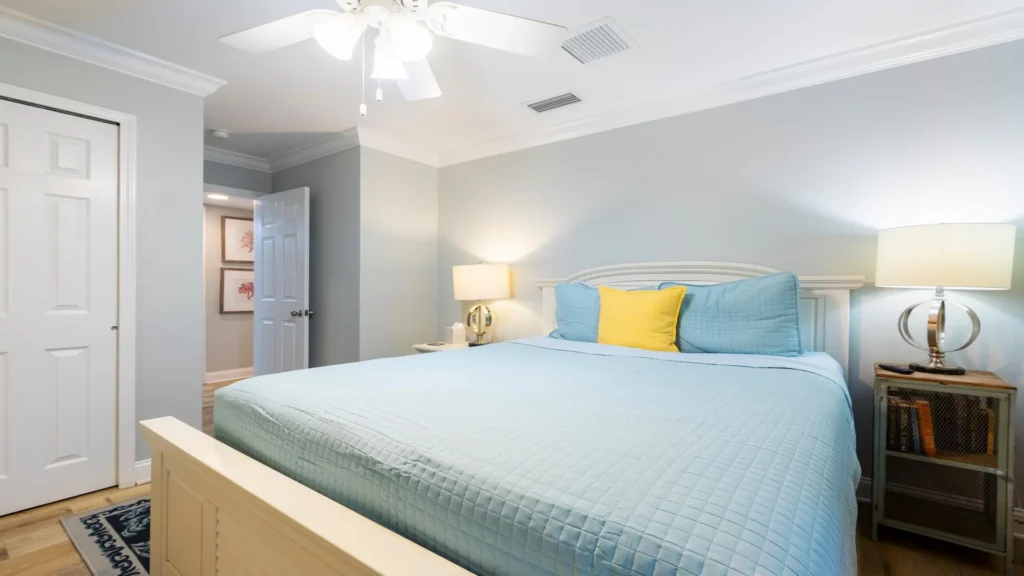 Guest King bedroom with light blue quilt and yellow accent pillow, flanked by modern lamps on rustic nightstands.