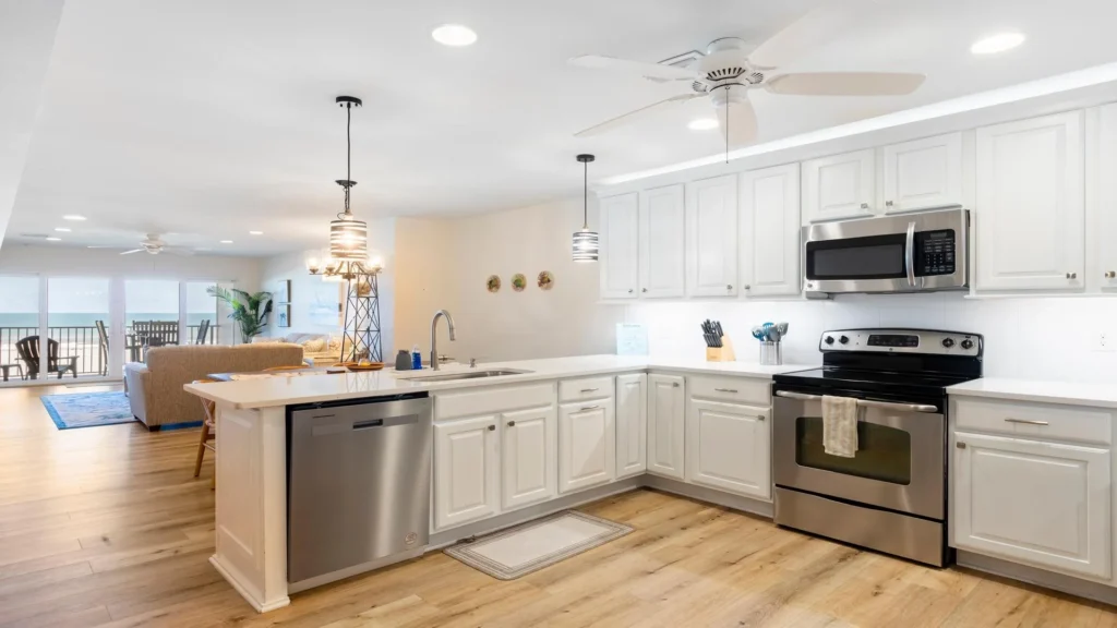 White cabinetry and stainless steel appliances wrap around the kitchen’s light wood flooring and quartz countertops.