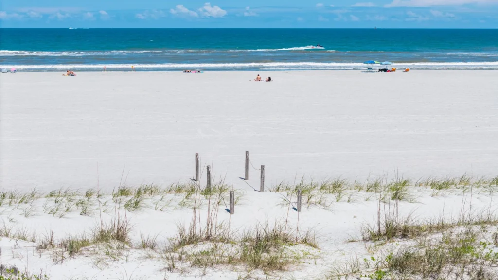 Sandy beach with sparse dune grass and wooden posts leading toward the blue Atlantic Ocean horizon.