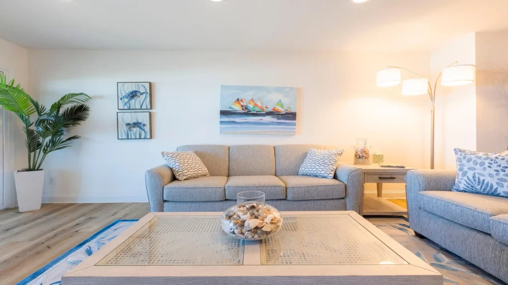 Living room with light gray sofas, patterned blue-and-white throw pillows, coastal artwork, and arched floor lamp.