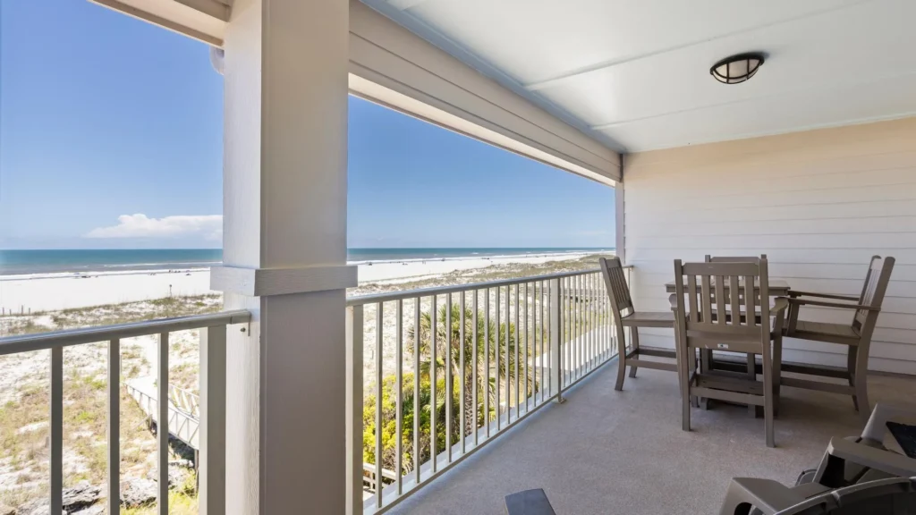 Covered balcony with wooden dining set, metal railing, and expansive views of the sandy beach and ocean horizon.