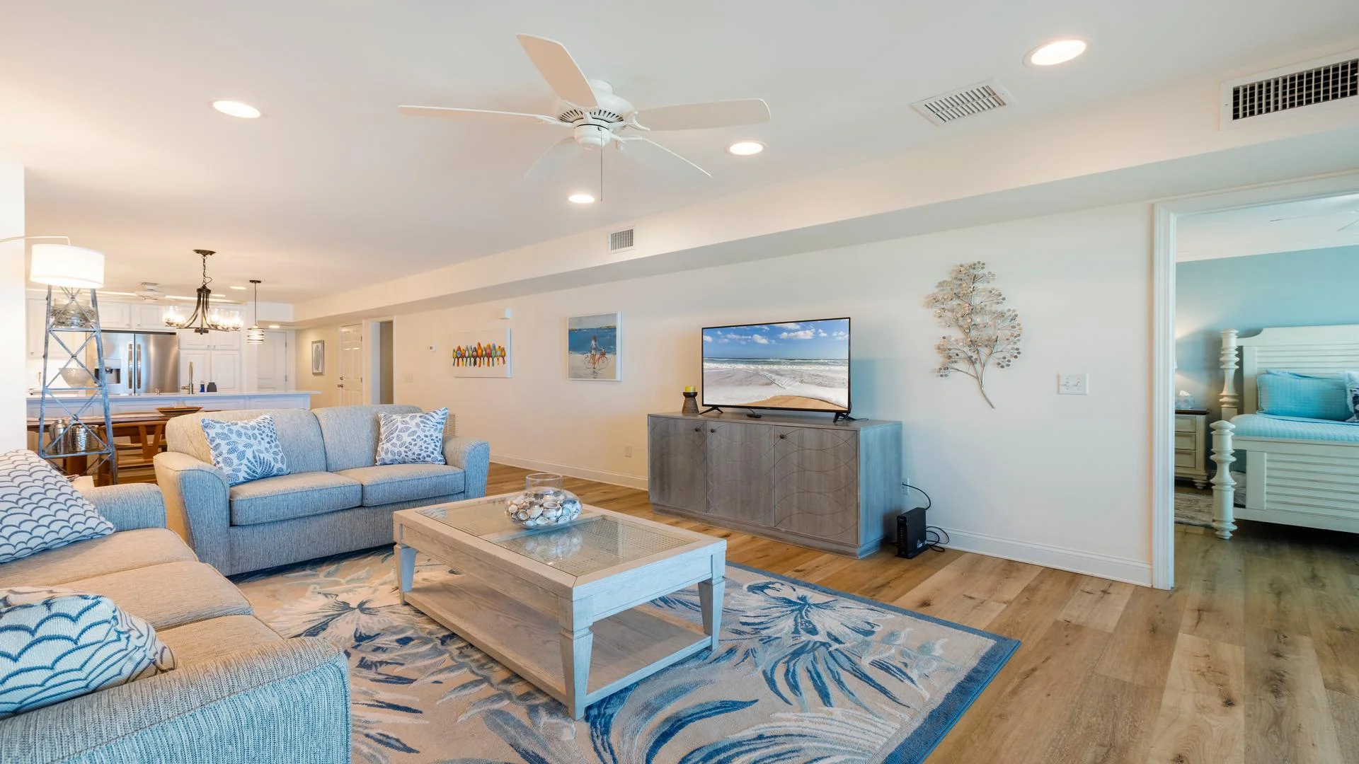 Living room with light gray sofas, a patterned blue area rug, wood coffee table, and flat-screen TV on blue-gray cabinet.