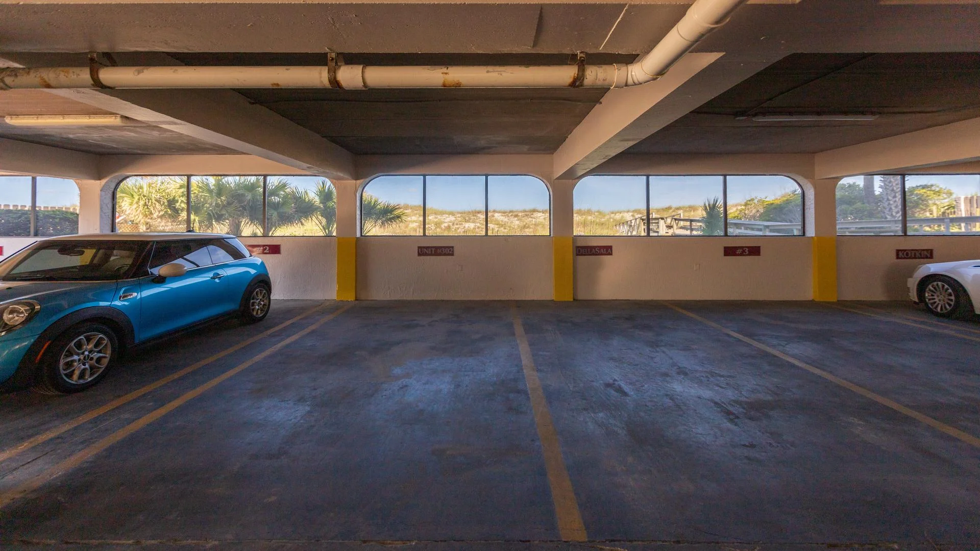 Covered parking space marked Unit #302 with concrete floor, arched windows, and yellow safety stripes.