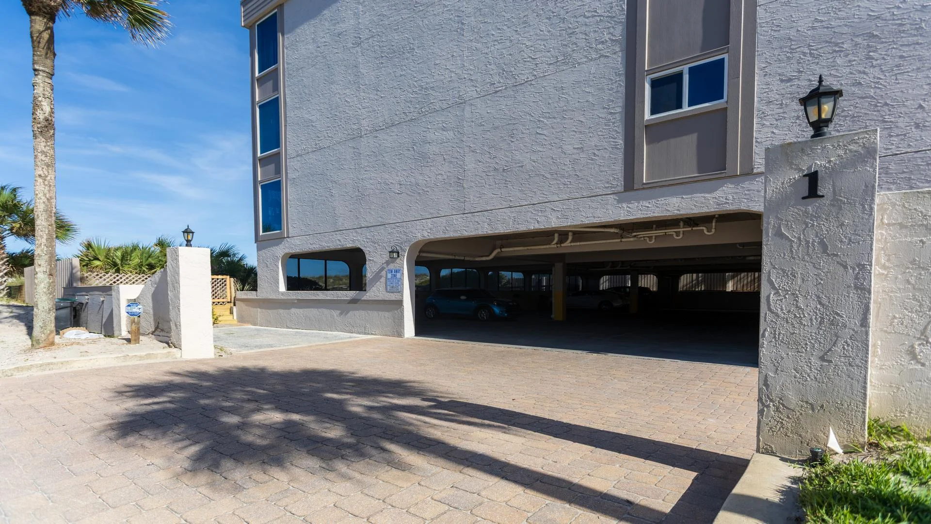 Entrance to covered parking under the condo with textured stucco walls, square pillars, and a paved driveway.