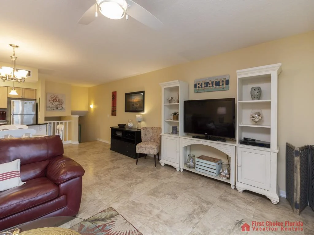 Entertainment center with white cabinetry and decorative shells flanks a flat-screen TV in the living area with beige walls and tile flooring.