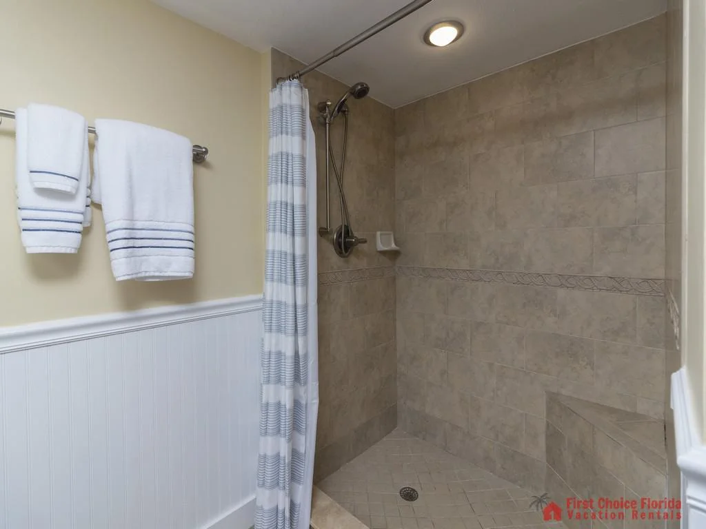 Walk-in shower with beige tile surround, built-in corner bench, and striped fabric curtain.