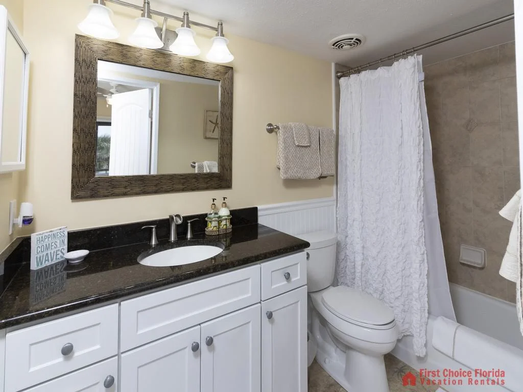 Bathroom features a white vanity with black granite countertop, large framed mirror, and tub-shower combination with textured white curtain.