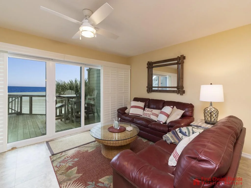Two maroon leather sofas face a glass-topped wicker coffee table in the living room with sliding doors to a deck overlooking the ocean.