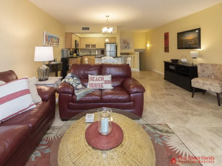 Wicker round coffee table with candle centerpiece sits atop a patterned area rug between leather sofas.