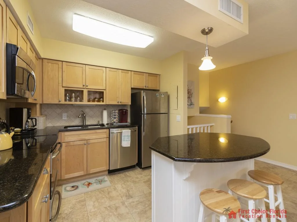 Kitchen with light wood cabinets, black granite countertops, stainless steel appliances, and a round island with wooden stools.