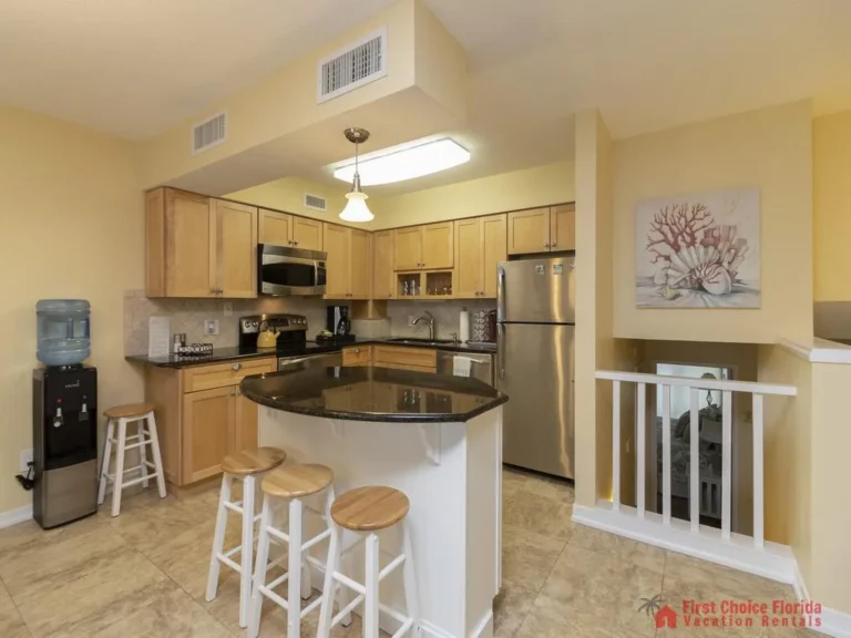 Kitchen with light wood cabinets, black granite island countertop, stainless steel appliances, and tiled floor.