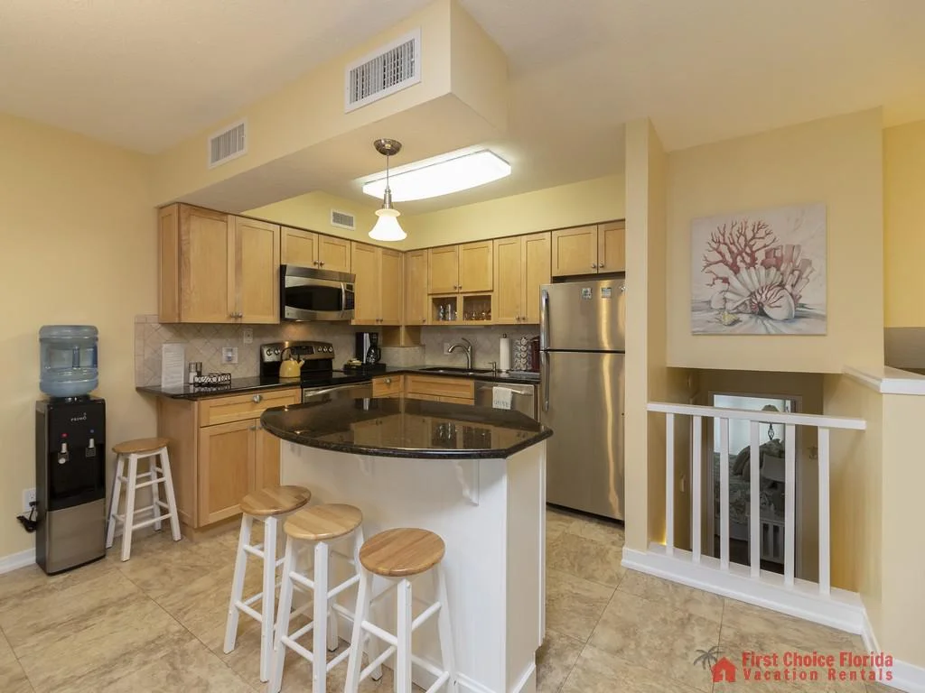 Kitchen with light wood cabinets, black granite island countertop, stainless steel appliances, and tiled floor.