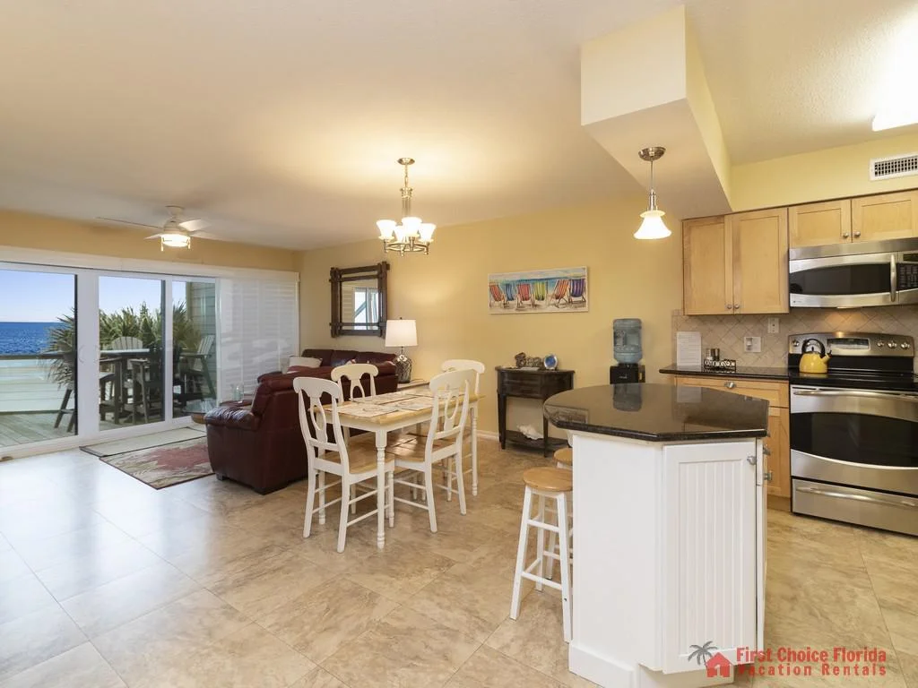 Kitchen island with black granite countertop faces a dining table and leather sofas near sliding glass doors to the balcony.