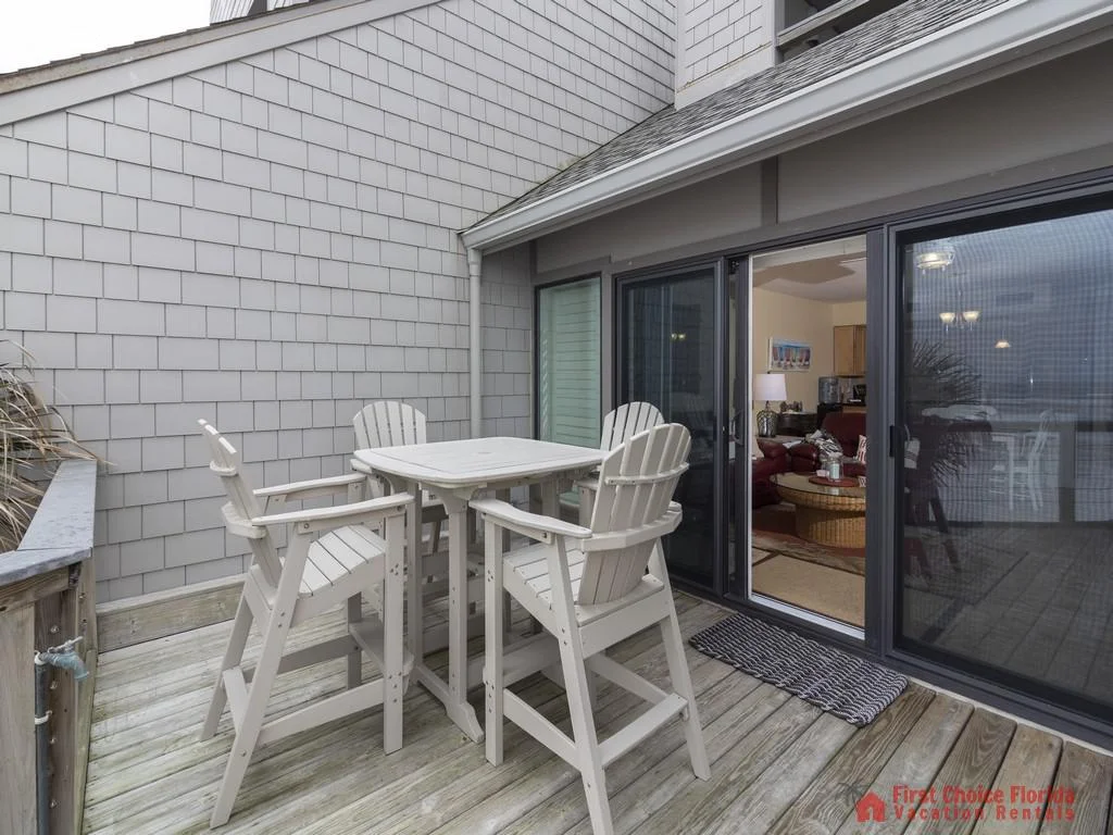 Wooden balcony with tall Adirondack chairs and square table faces sliding glass doors into the living room.