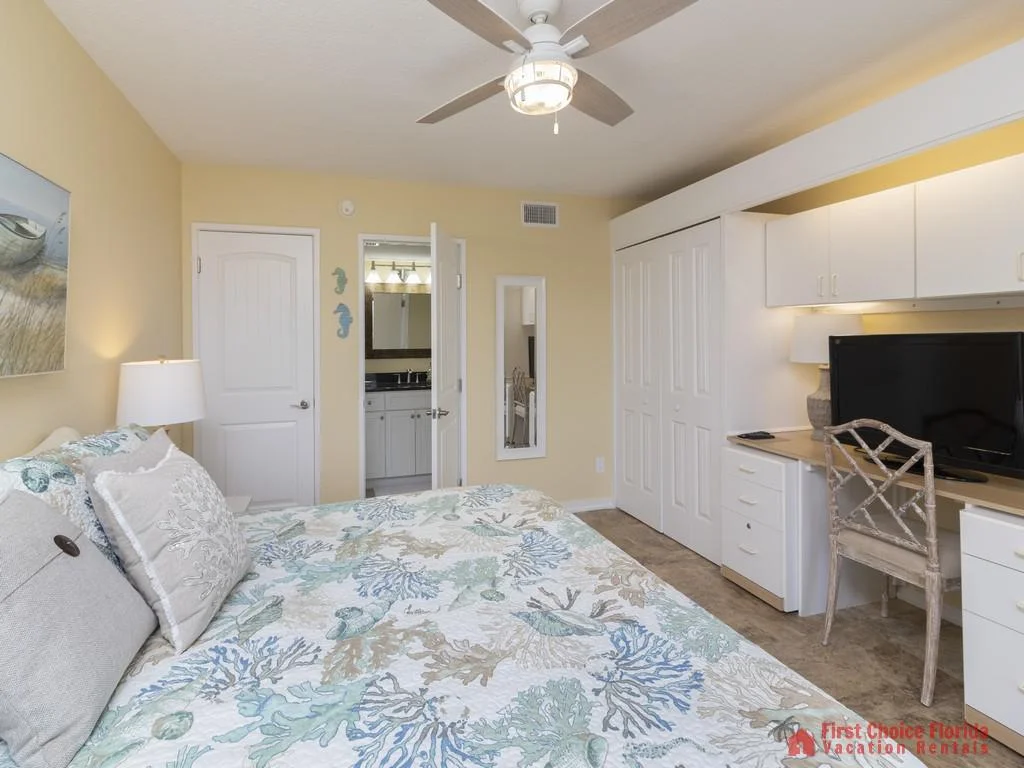 Built-in desk area with overhead cabinets, a flat-screen TV, and a wicker chair in the master bedroom.