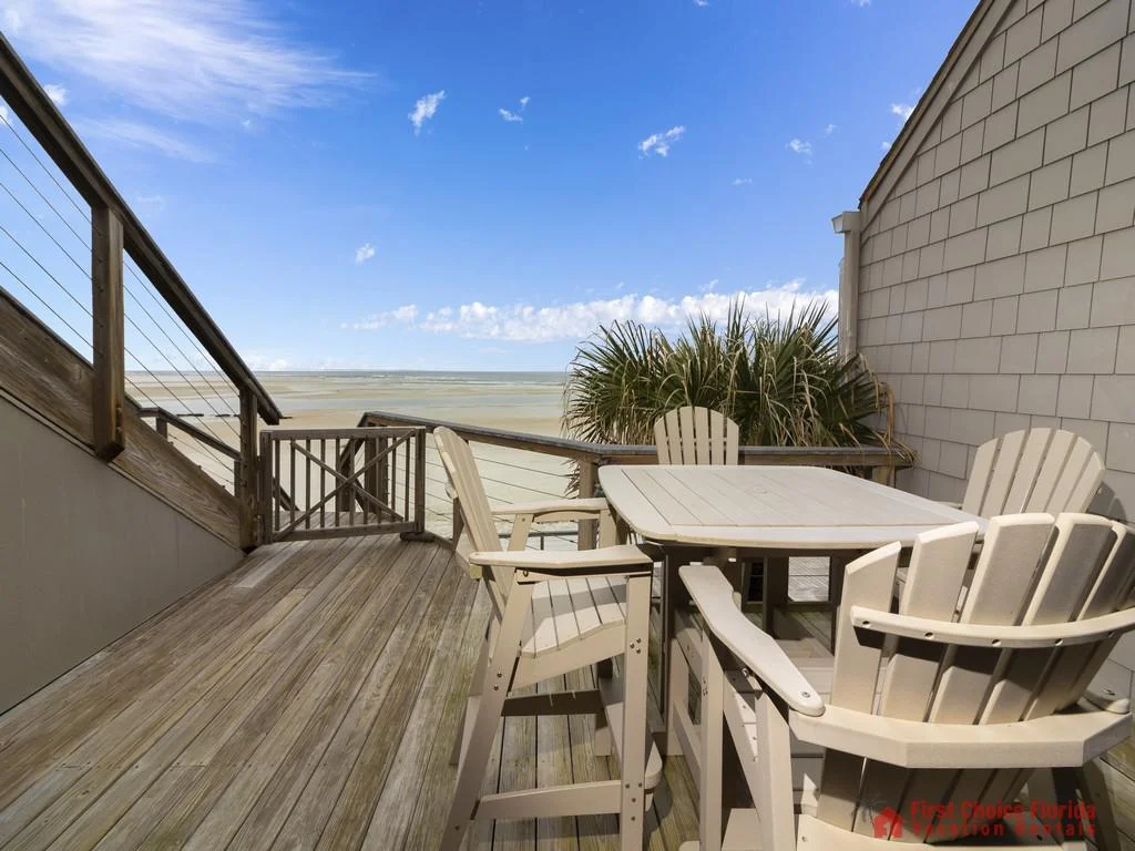 Outdoor balcony with weathered wood decking, beige Adirondack chairs, and a view of the ocean and sky.