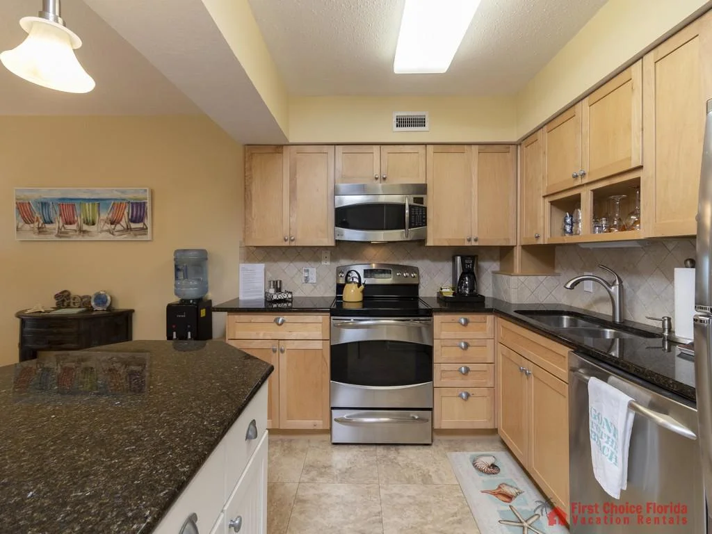 Light wood cabinetry and black granite countertops surround stainless steel appliances in the kitchen with tiled floors.