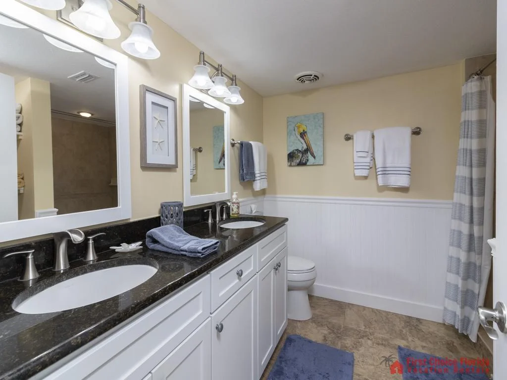 Double vanity with black granite countertop and white cabinetry under soft lighting in bathroom.