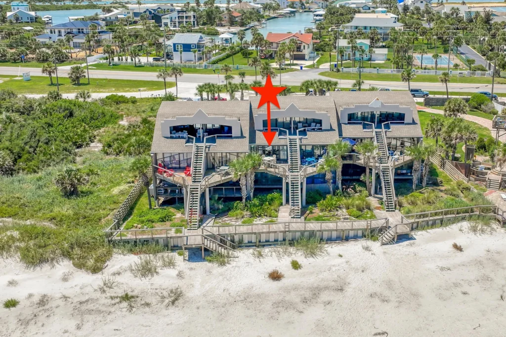 Exterior view of beachfront condos with wooden stairs and a boardwalk leading down to white sandy beach dunes.