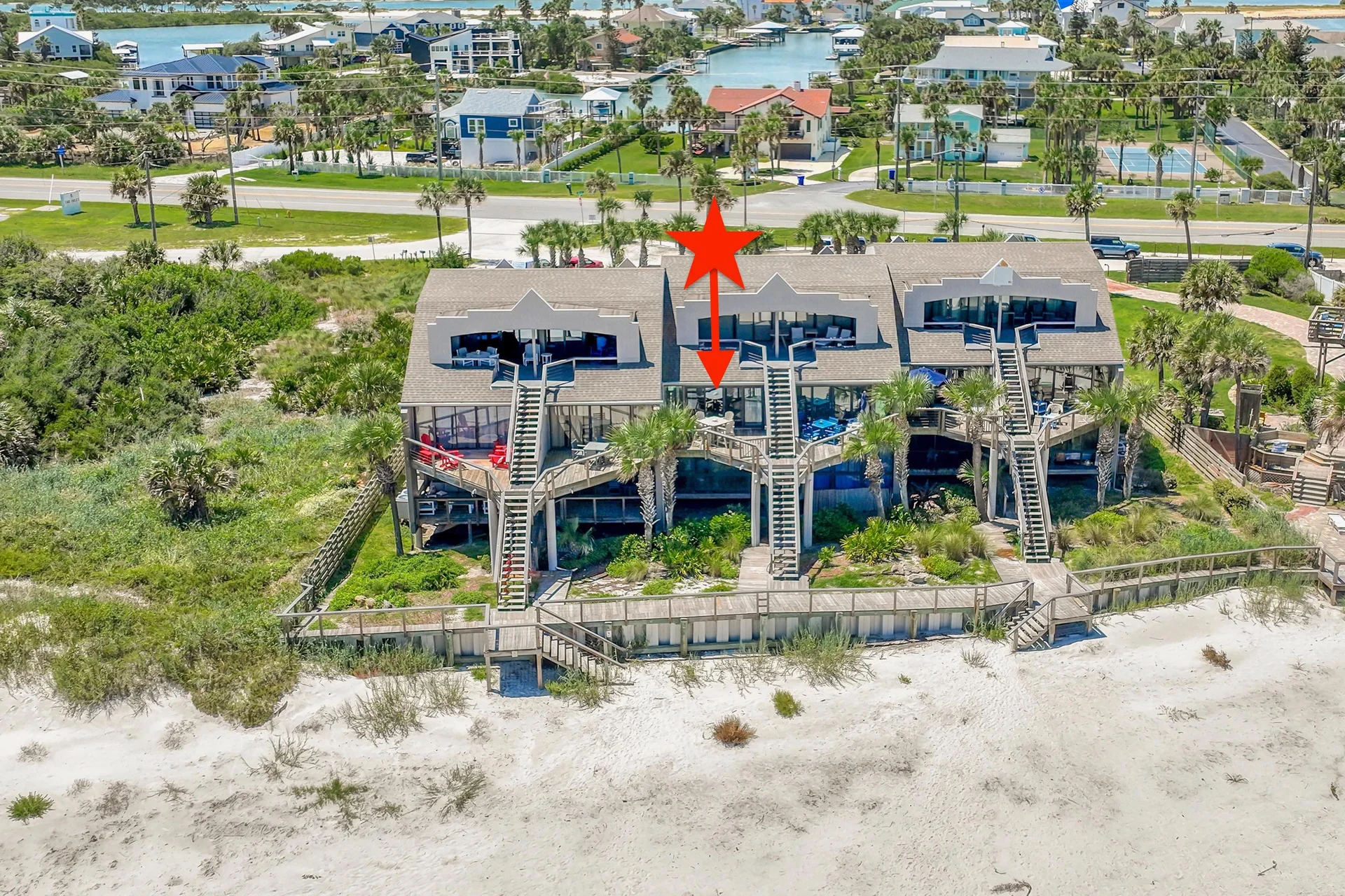 Exterior view of beachfront condos with wooden stairs and a boardwalk leading down to white sandy beach dunes.