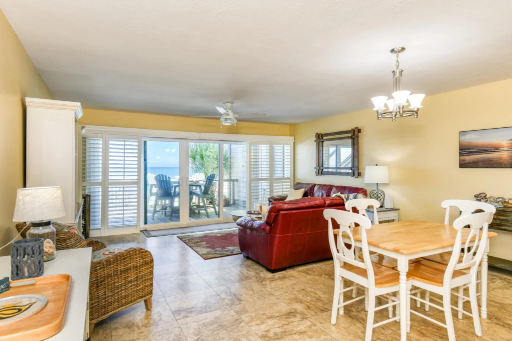 Open living and dining area with tile floors, white dining set, red leather sofa, and ocean views through sliding glass doors.