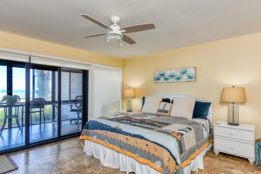 King bed with lighthouse-themed quilt rests between white nightstands topped with glass table lamps.