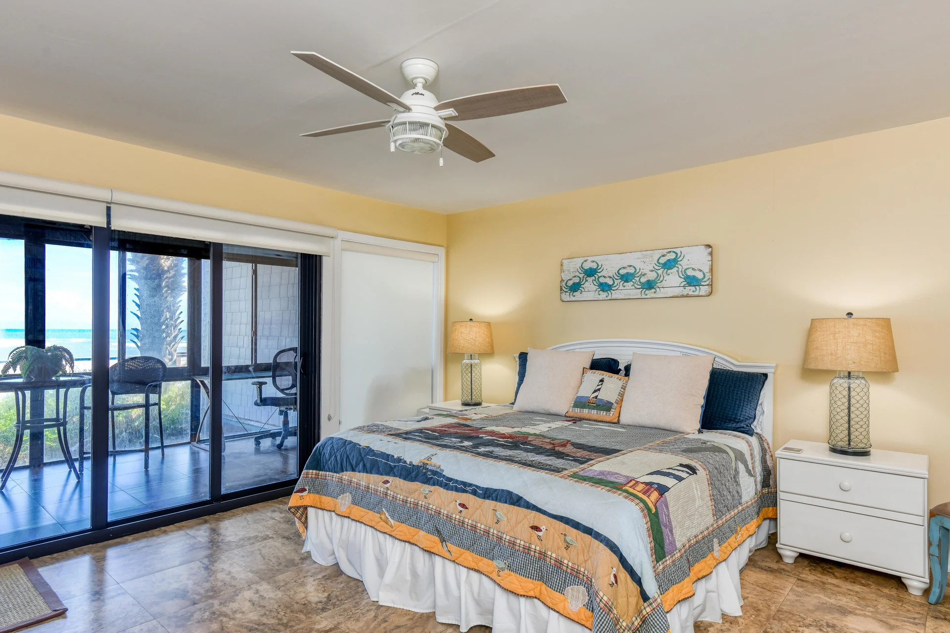 King bed with lighthouse-themed quilt rests between white nightstands topped with glass table lamps.