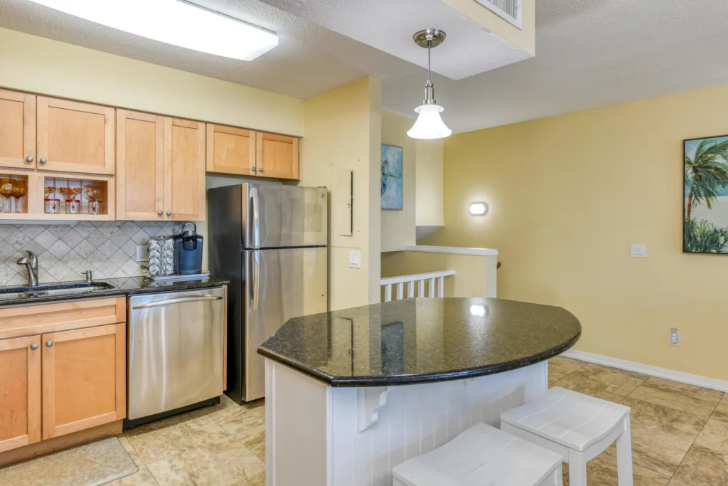 Kitchen area with light wood cabinets, stainless steel appliances, granite countertop island, and tiled flooring.