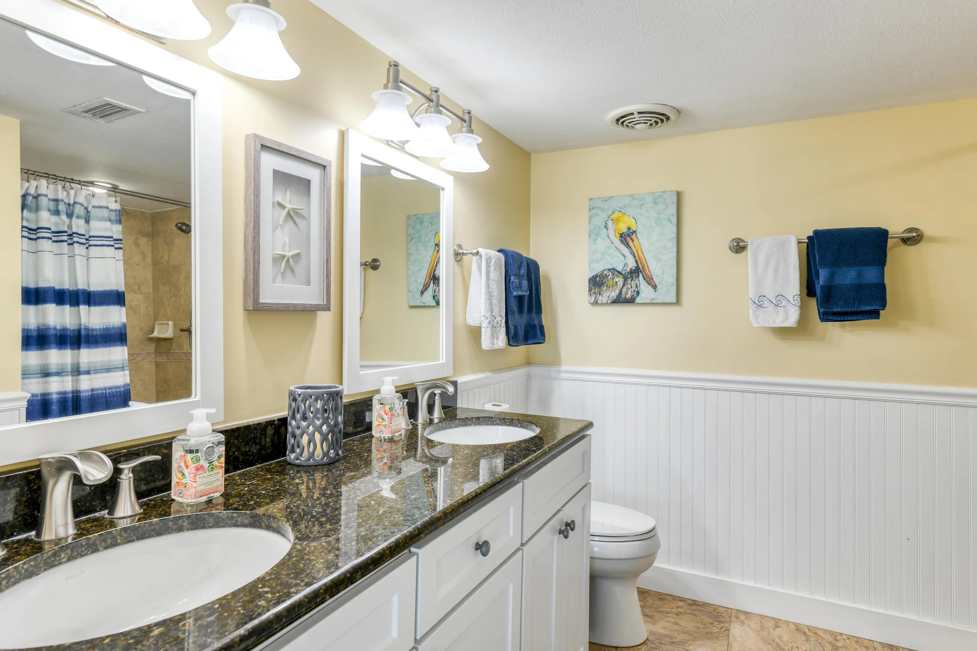 Bathroom features a double sink with dark granite countertop, white cabinetry, and coastal-themed wall art.