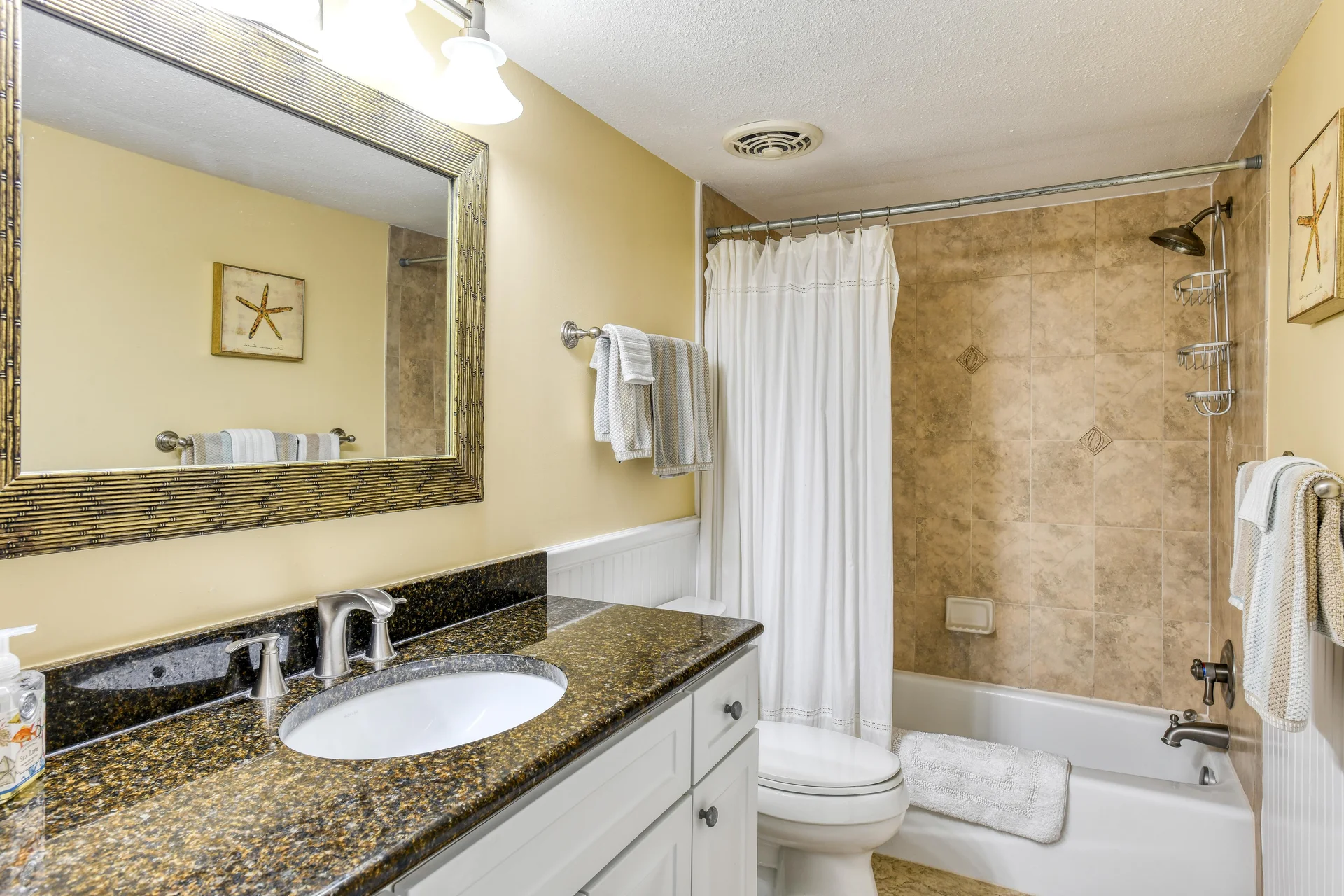 Bathroom featuring a granite countertop vanity, white cabinetry, and a tub with beige tiled surround and shower curtain.